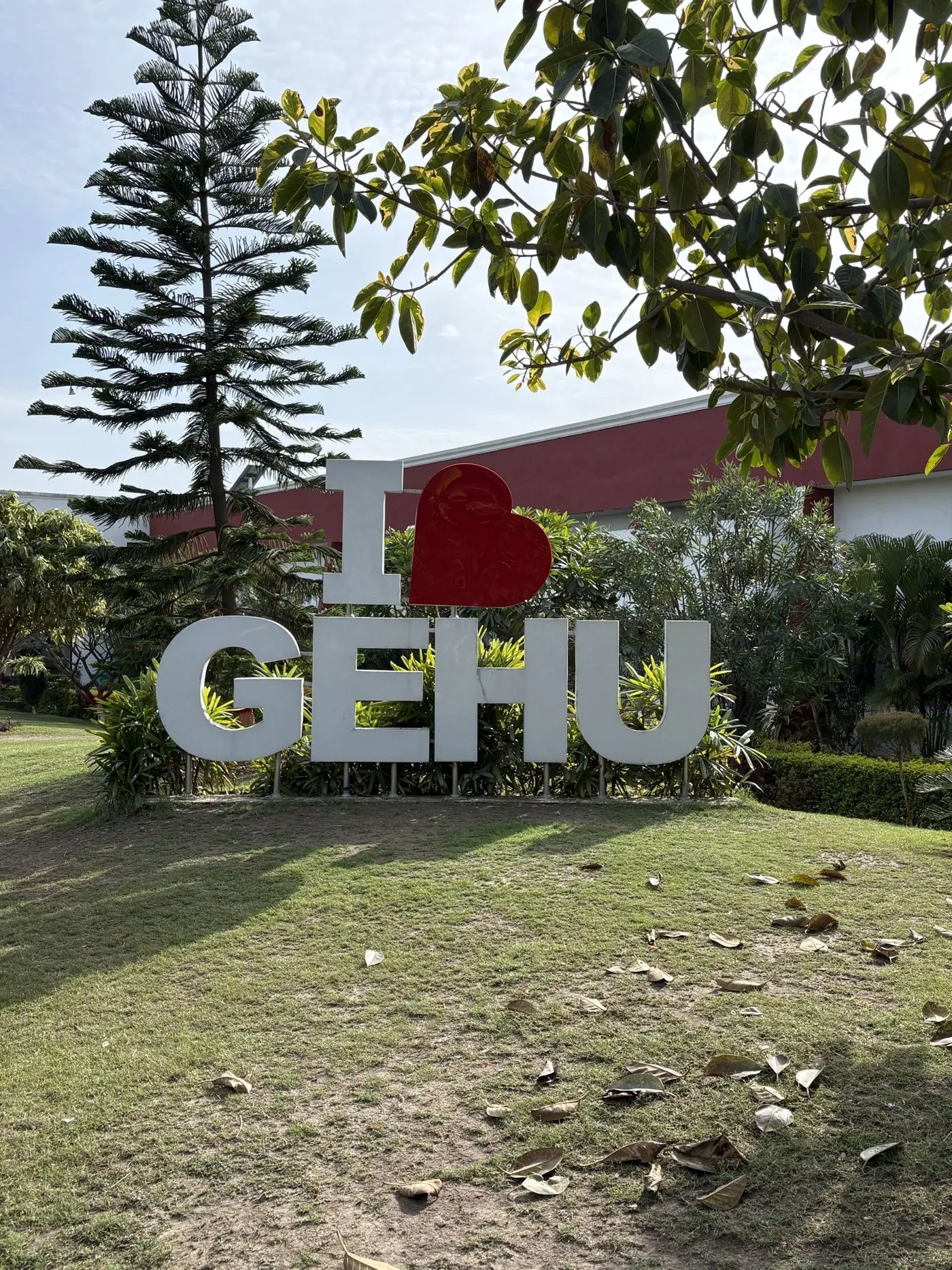 The I love GEHU sign on a lawn in front of a red campus building